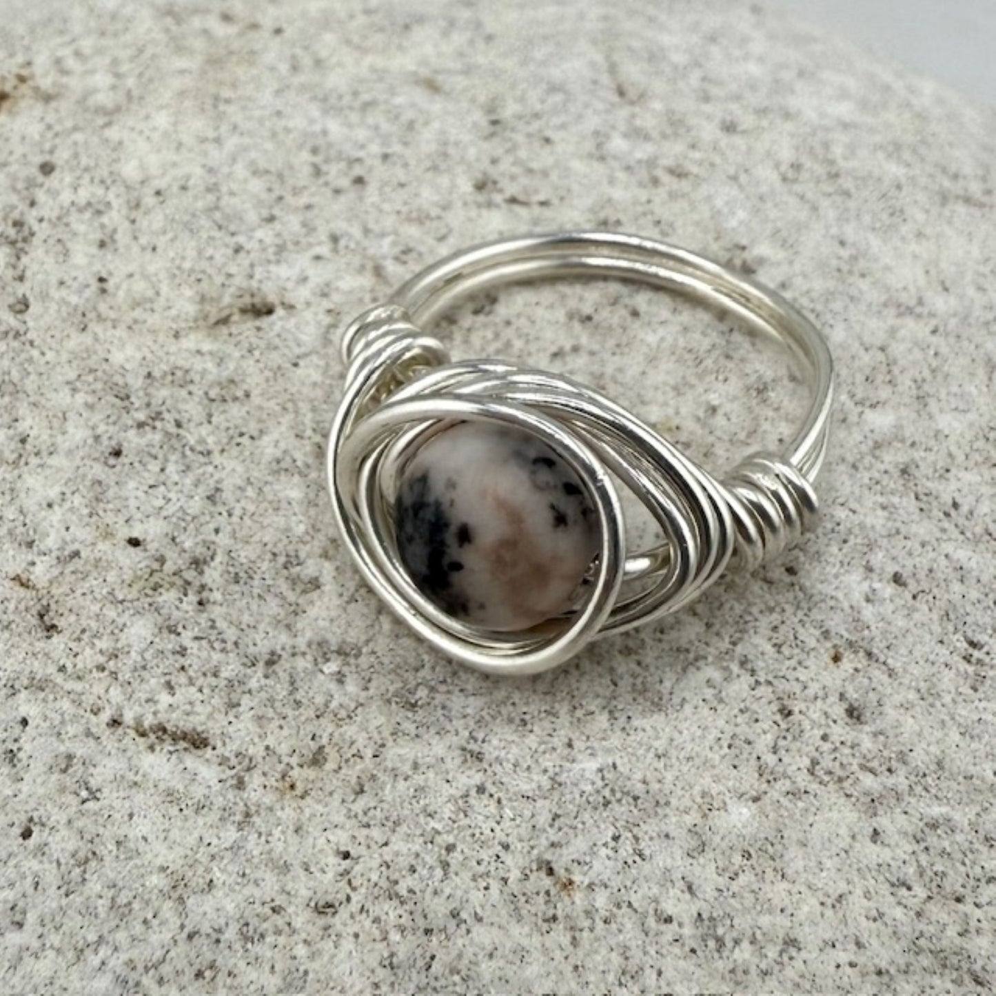 Silver wire-wrapped ring with a natural stone on a textured surface