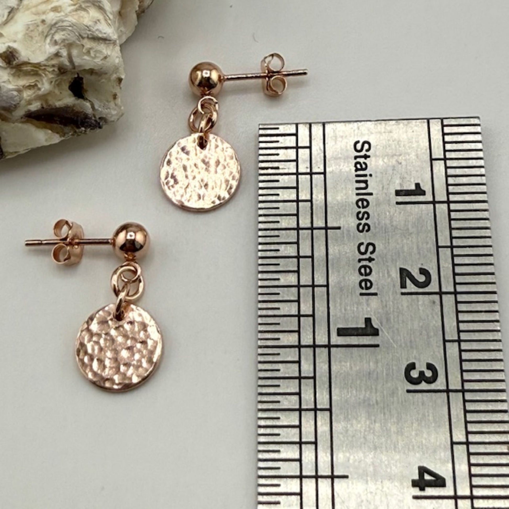 Rose gold stud earrings with round discs next to a ruler for size reference.