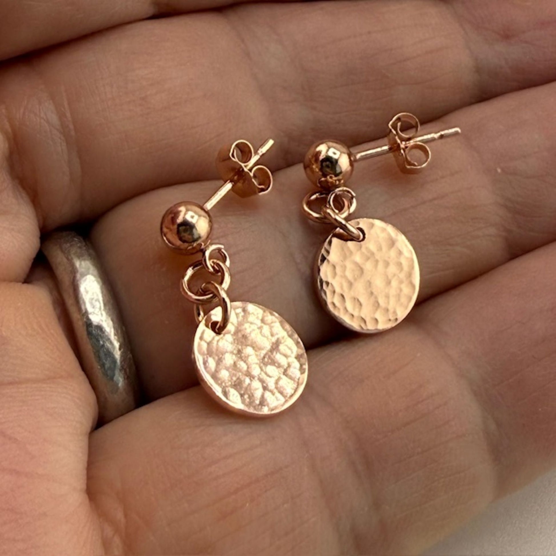 Rose gold stud earrings with round discs held between fingers