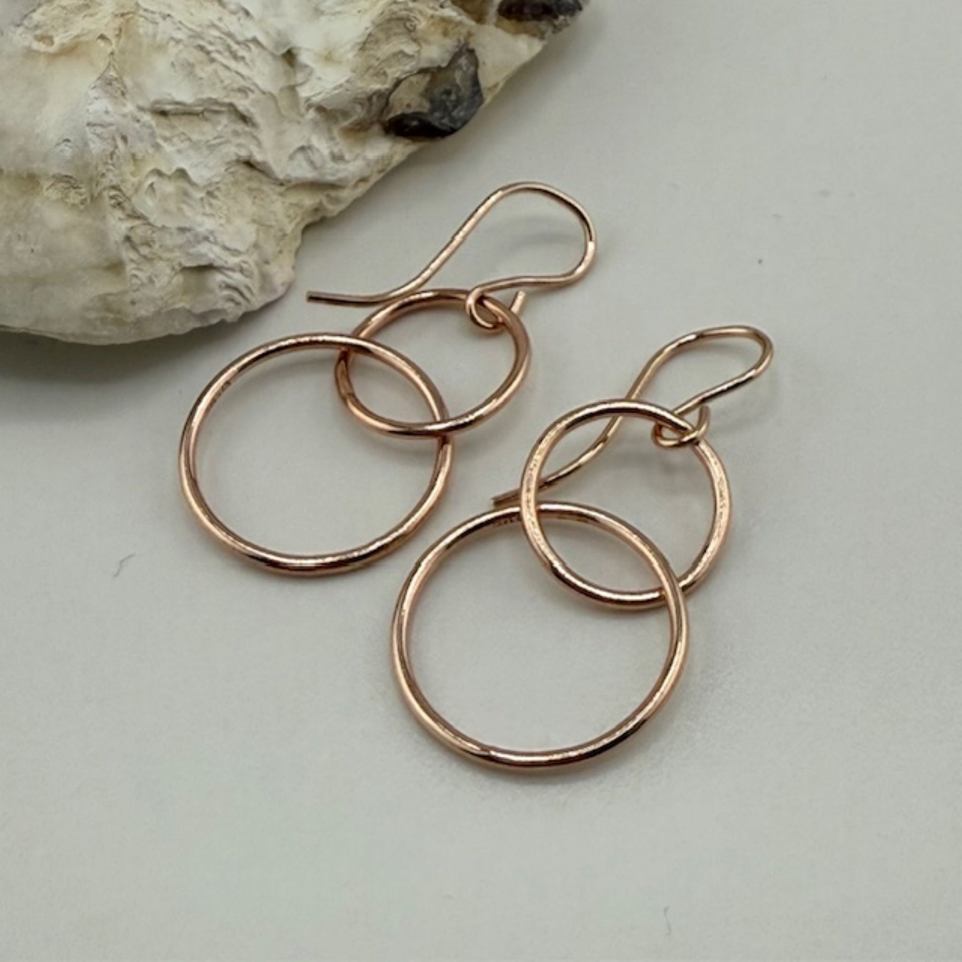 Rose gold hoop earrings on a light gray surface with a stone in the background