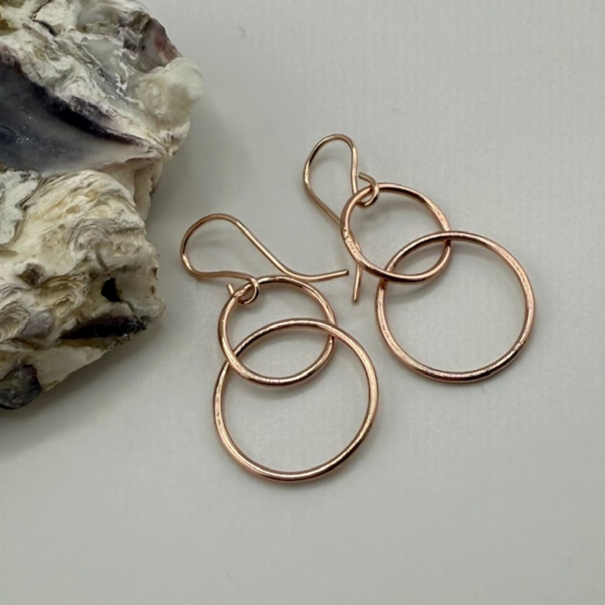 Rose gold hoop earrings on a light gray surface with a rock in the background