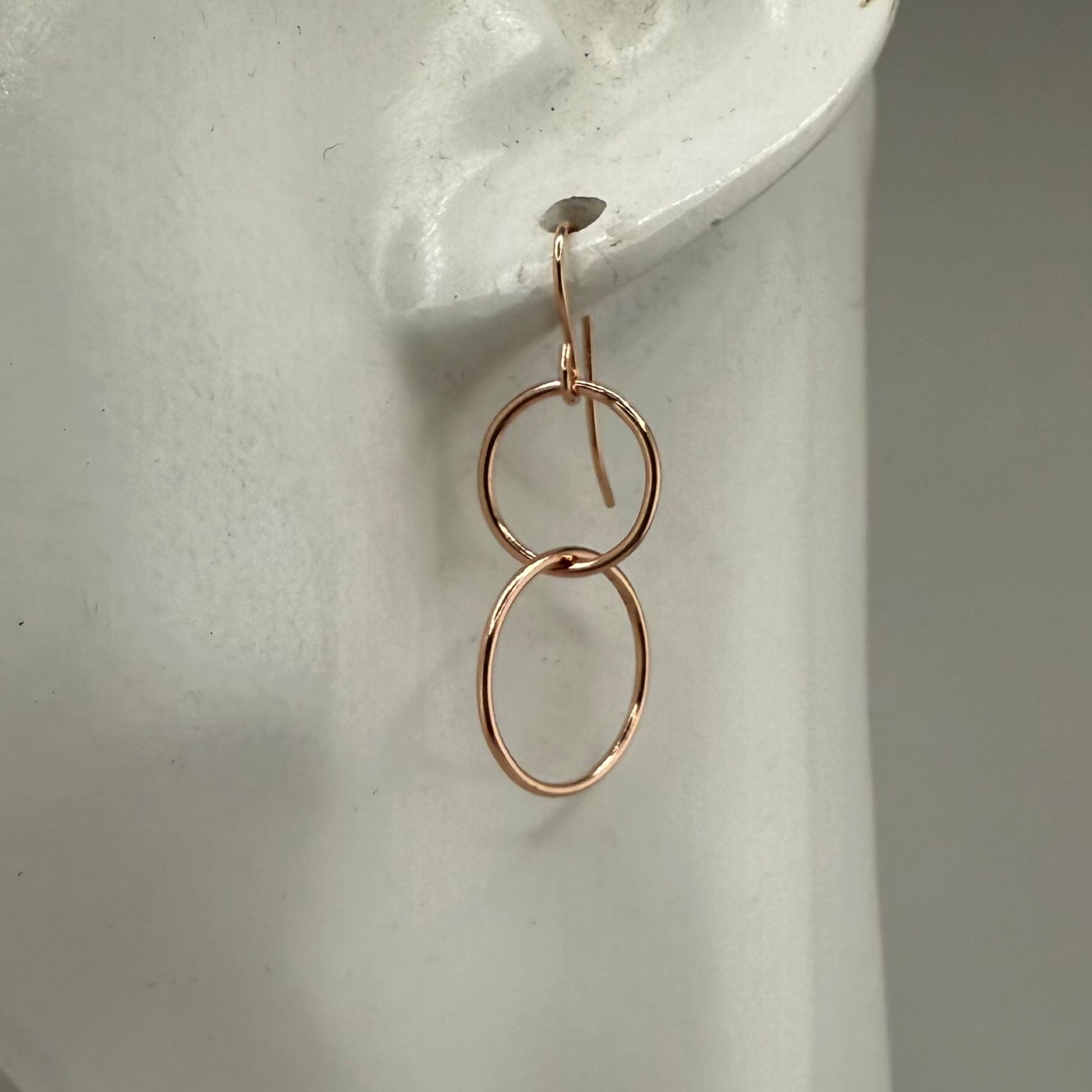 Rose gold double-circle earring on a white display stand with a neutral background