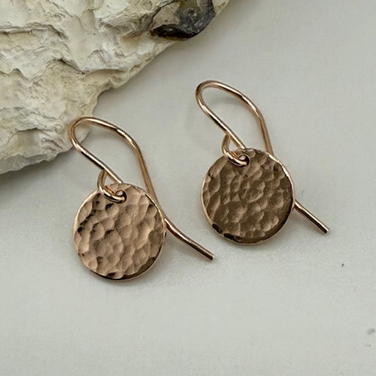 Pair of rose gold earrings on a light surface with a stone background