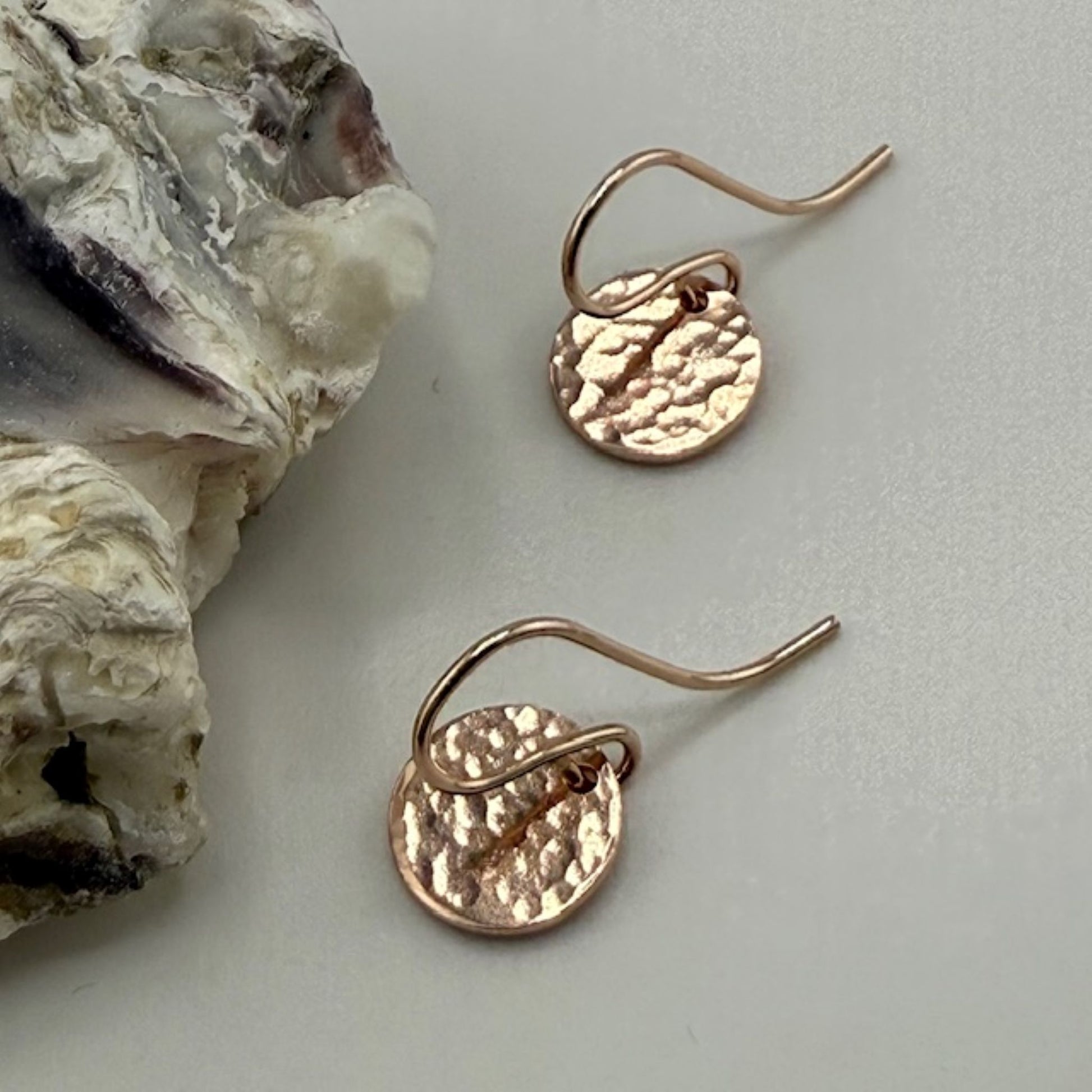 Rose gold earrings on a light gray surface with a natural rock formation.