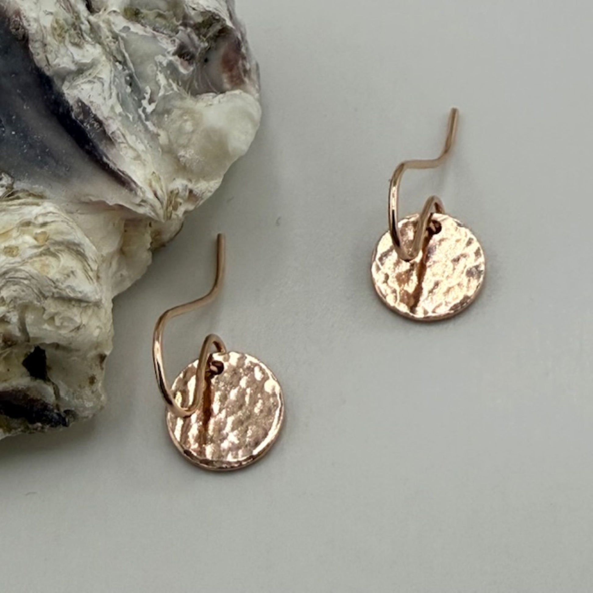 Rose gold earrings on a light gray surface with a textured rock in the background