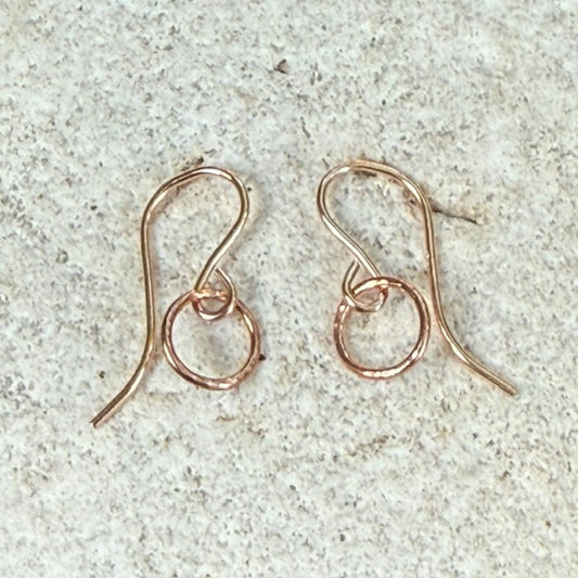 Rose gold hoop circle earrings on a textured stone surface