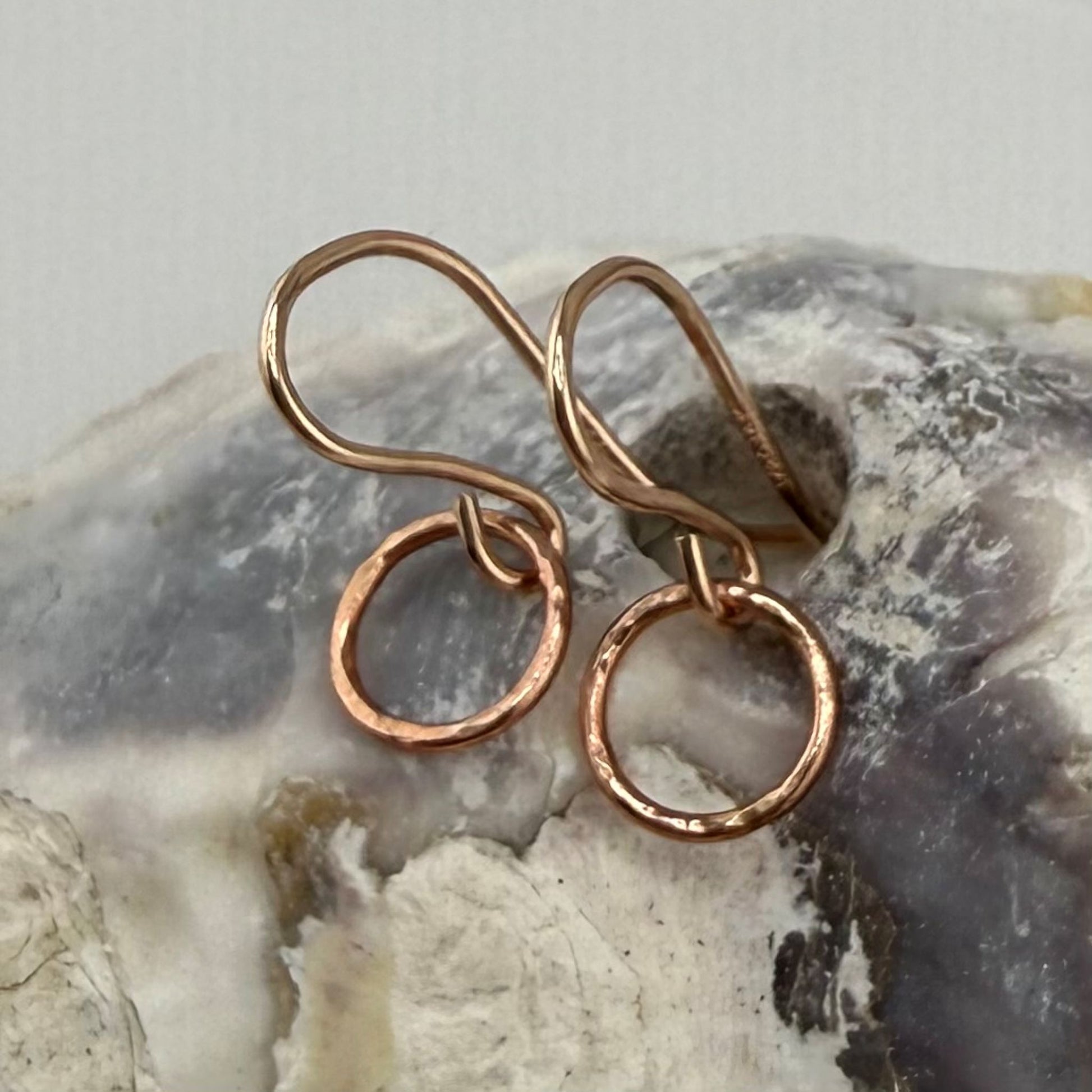 Pair of rose gold circle hoop earrings on a textured stone surface