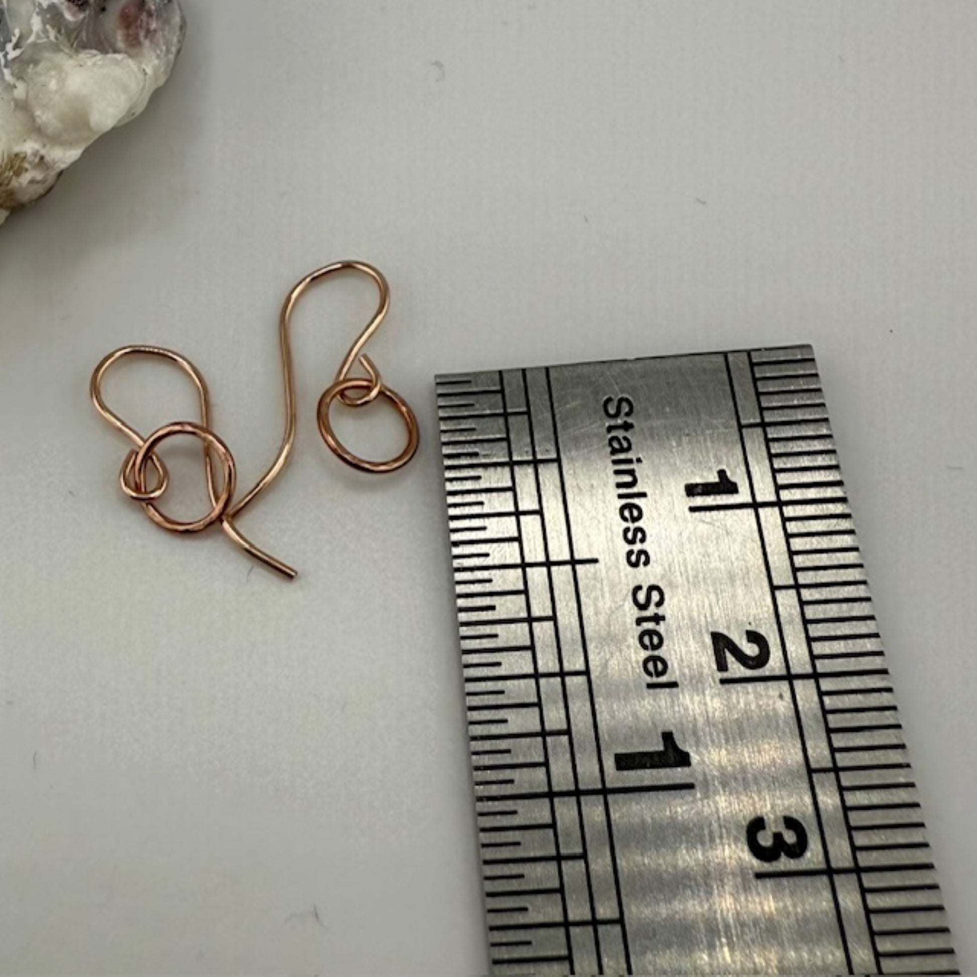 Rose gold circle hoop earrings next to a stainless steel ruler on a white surface