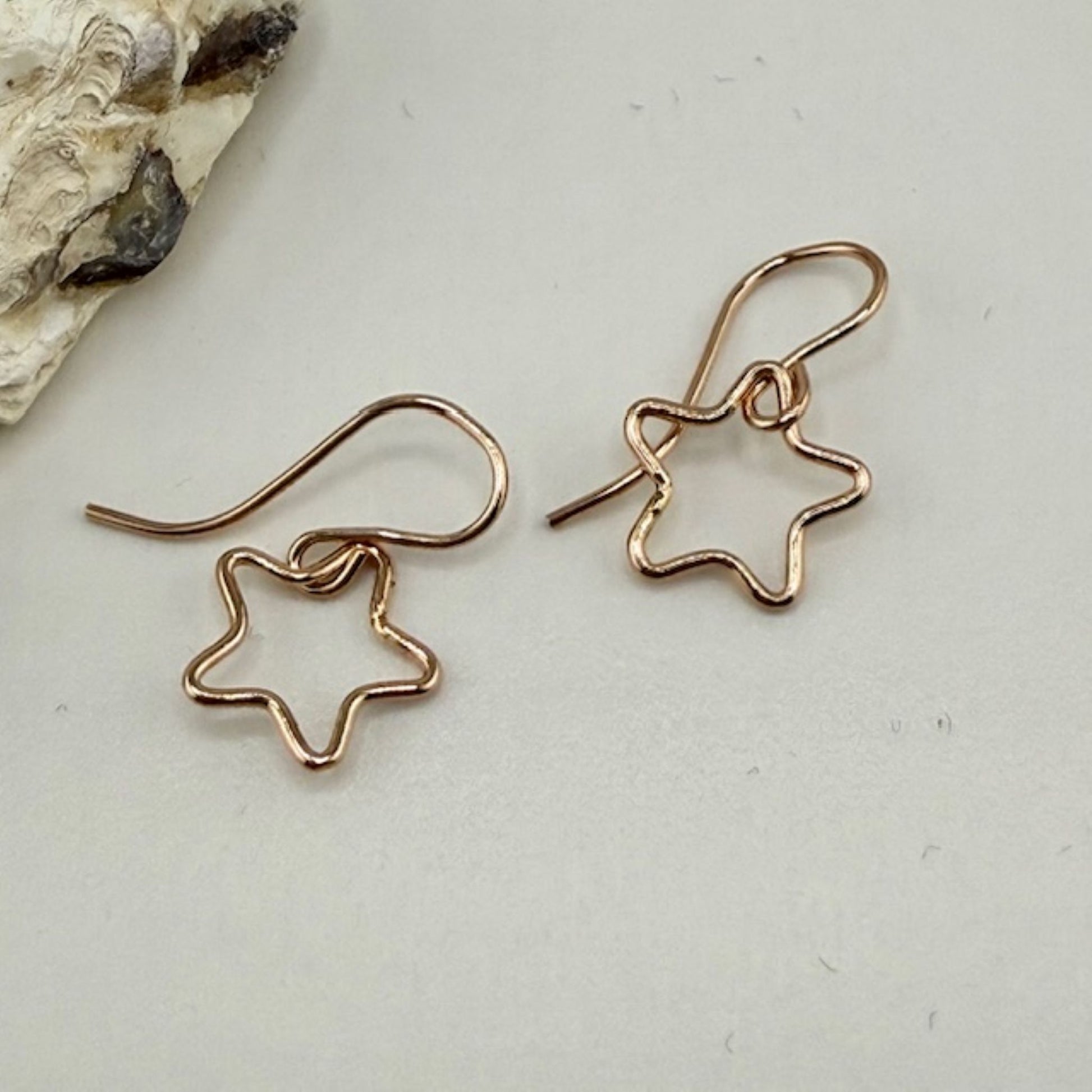 Star-shaped rose gold earrings on a light gray surface with a natural rock background.