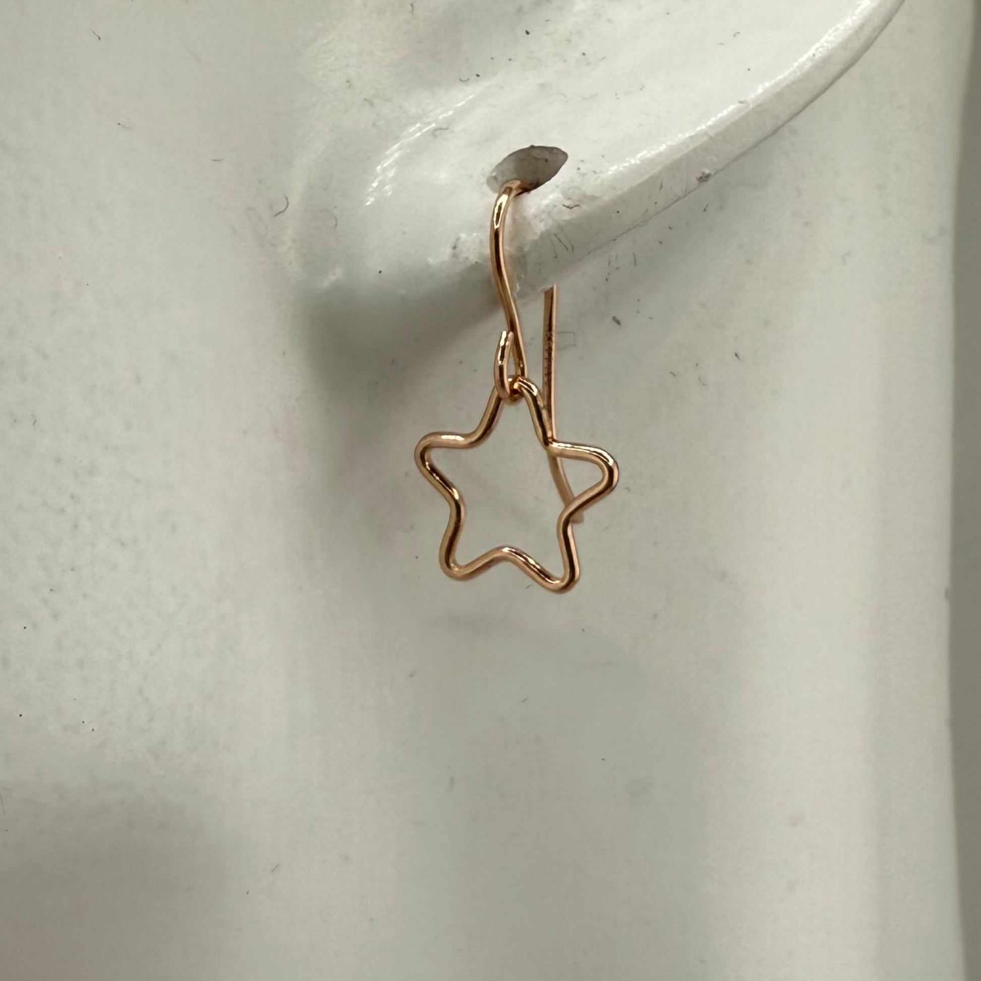 Rose gold star-shaped earring on a white ear marble display 