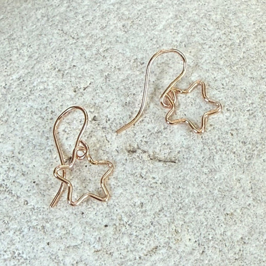 Star-shaped rose gold earrings on a light gray stone surface