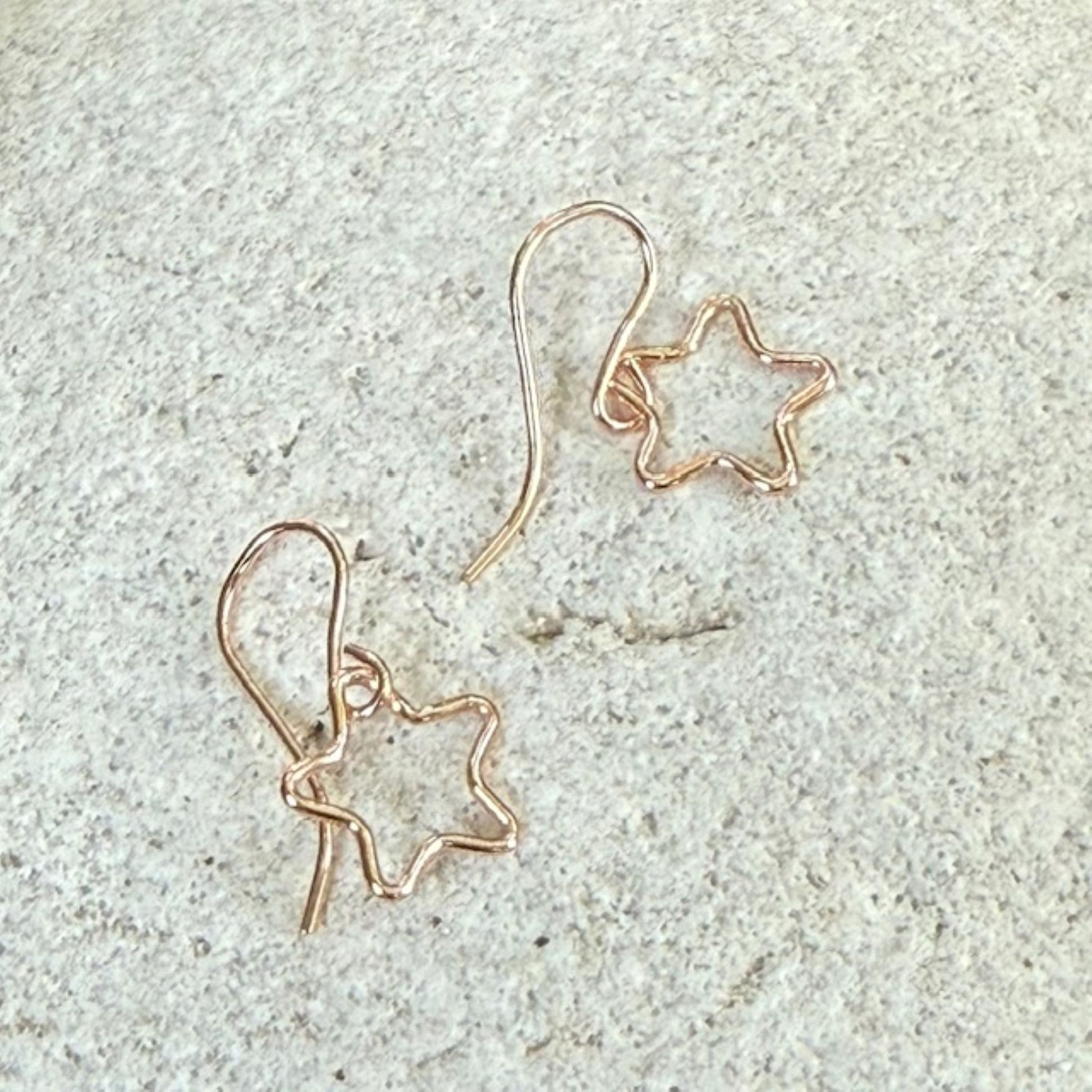 Pair of star-shaped rose gold earrings on a textured stone surface