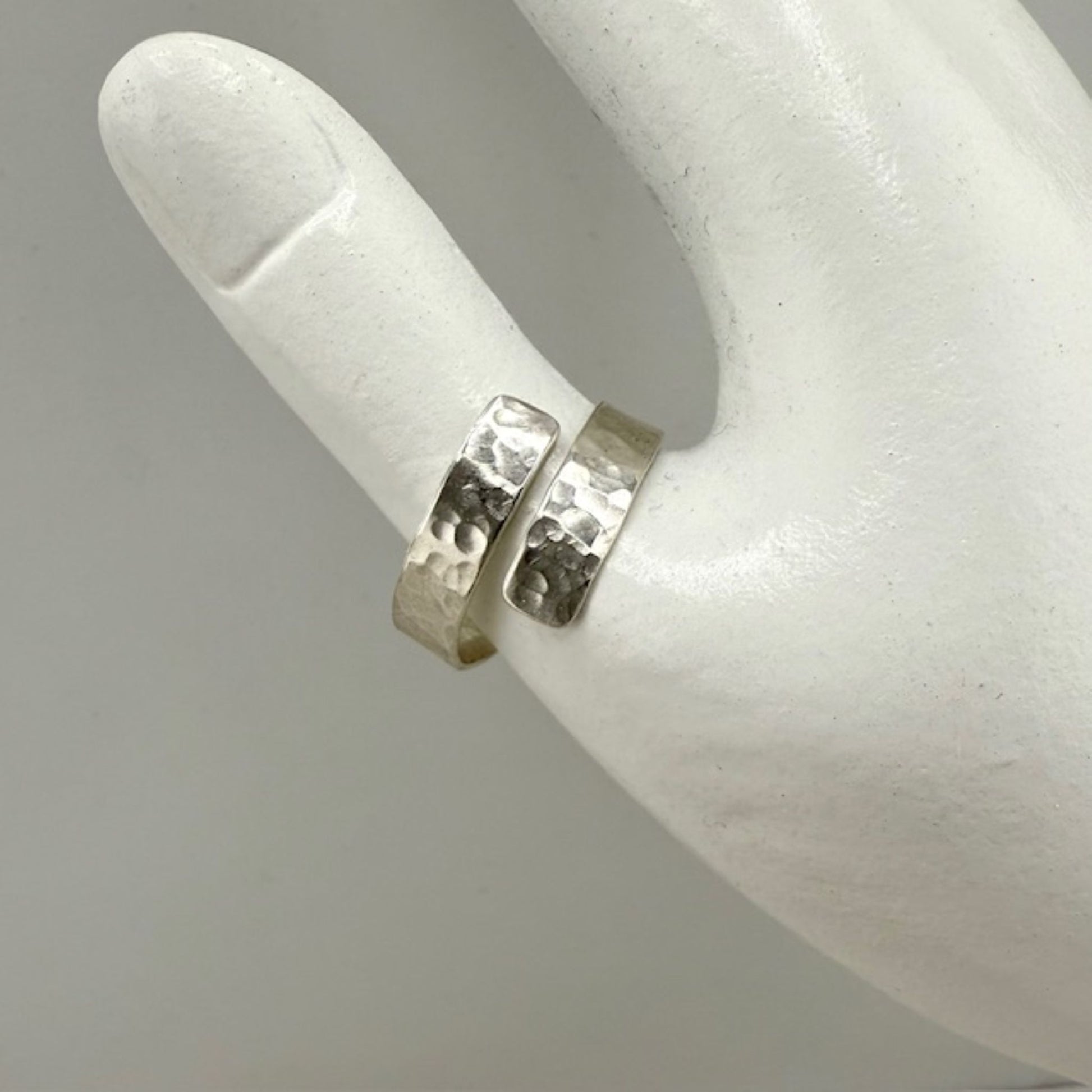 Silver ring with a textured design on a white mannequin finger.