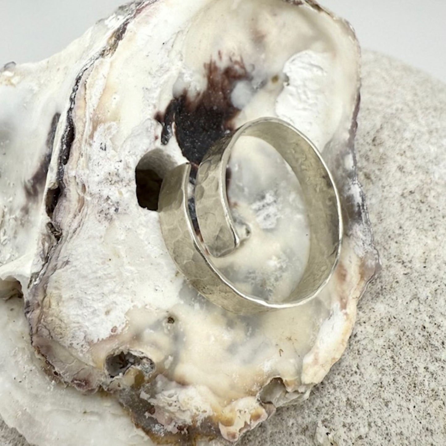 Silver ring on a white oyster shell with sand in the background