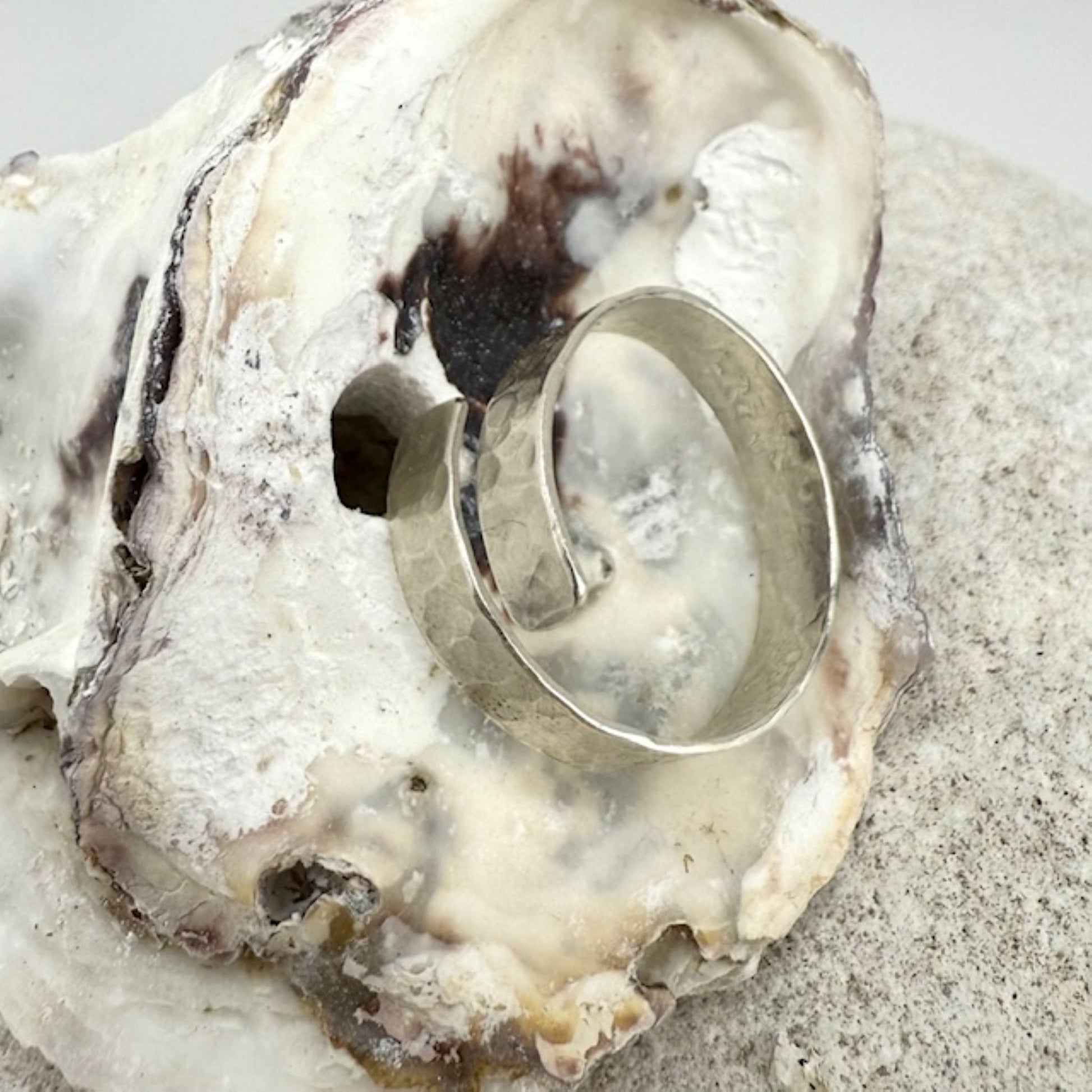 Silver ring on a white oyster shell with sand in the background