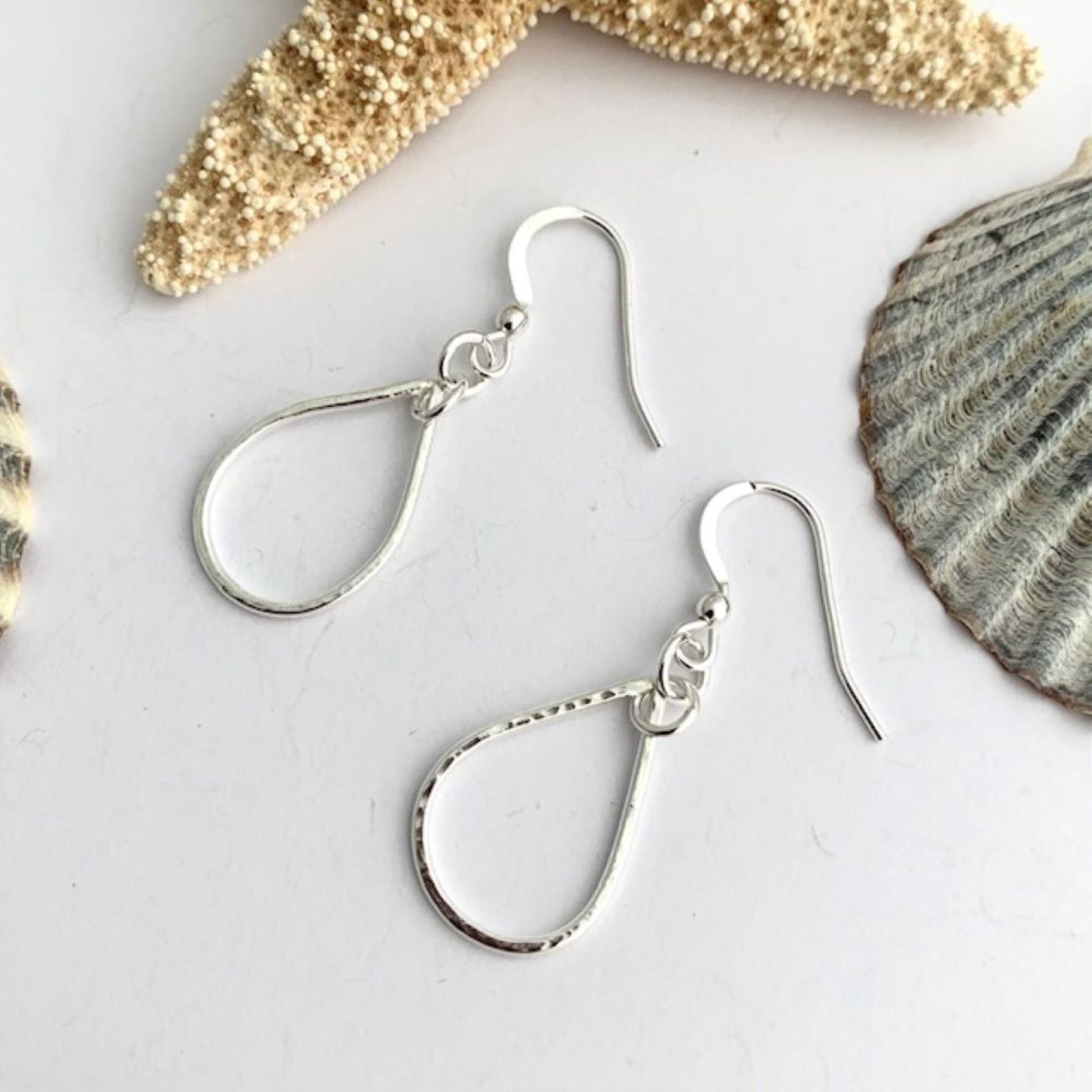 Sterling silver earrings on a light gray surface with seashells in the background