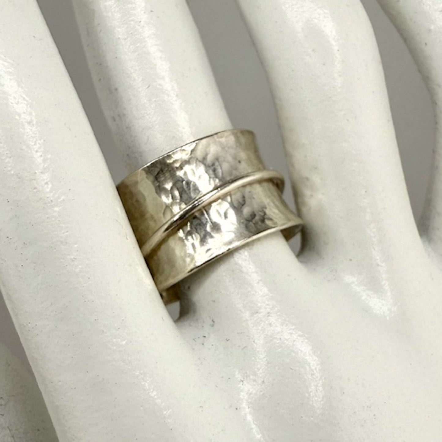 Silver spinner ring with a textured band on a white marble hand display