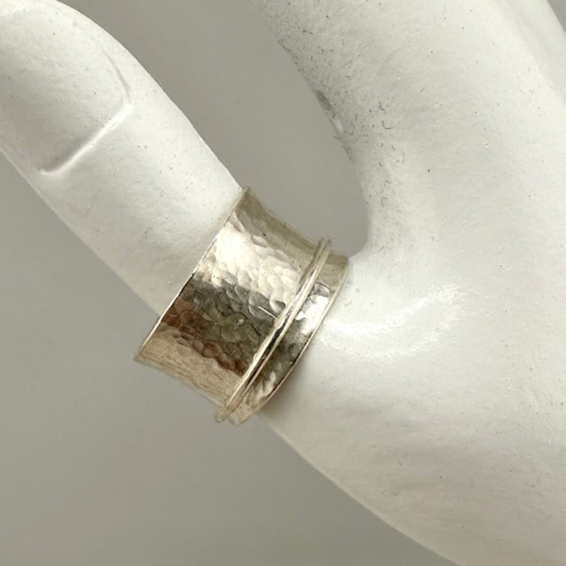Silver spinner ring with a textured band on a white marble hand display