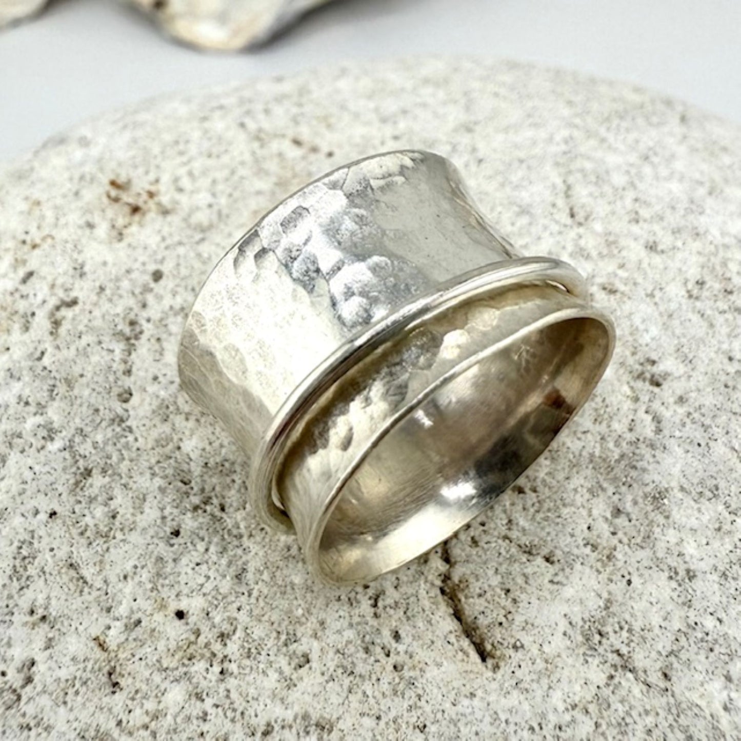 Silver spinner ring with textured surface on a stone background