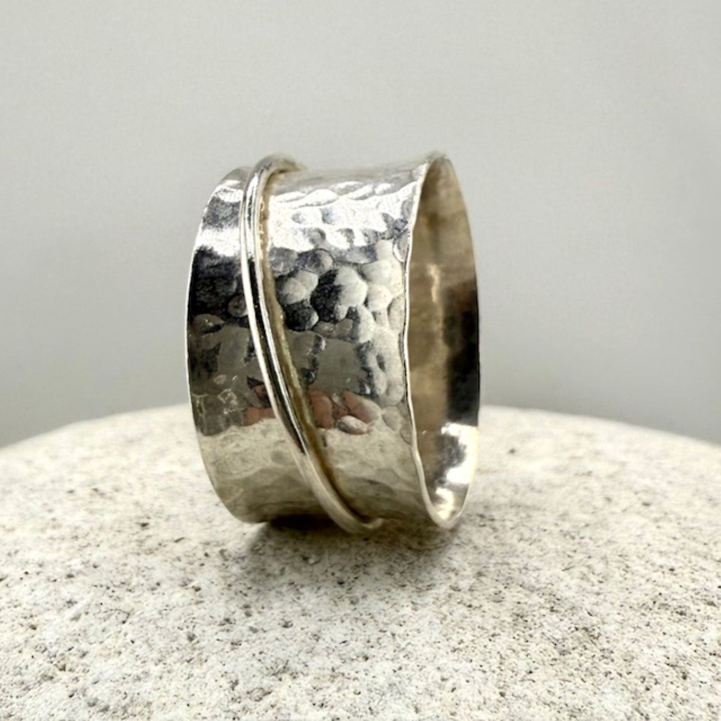 Silver spinner ring with a textured surface on a light gray background