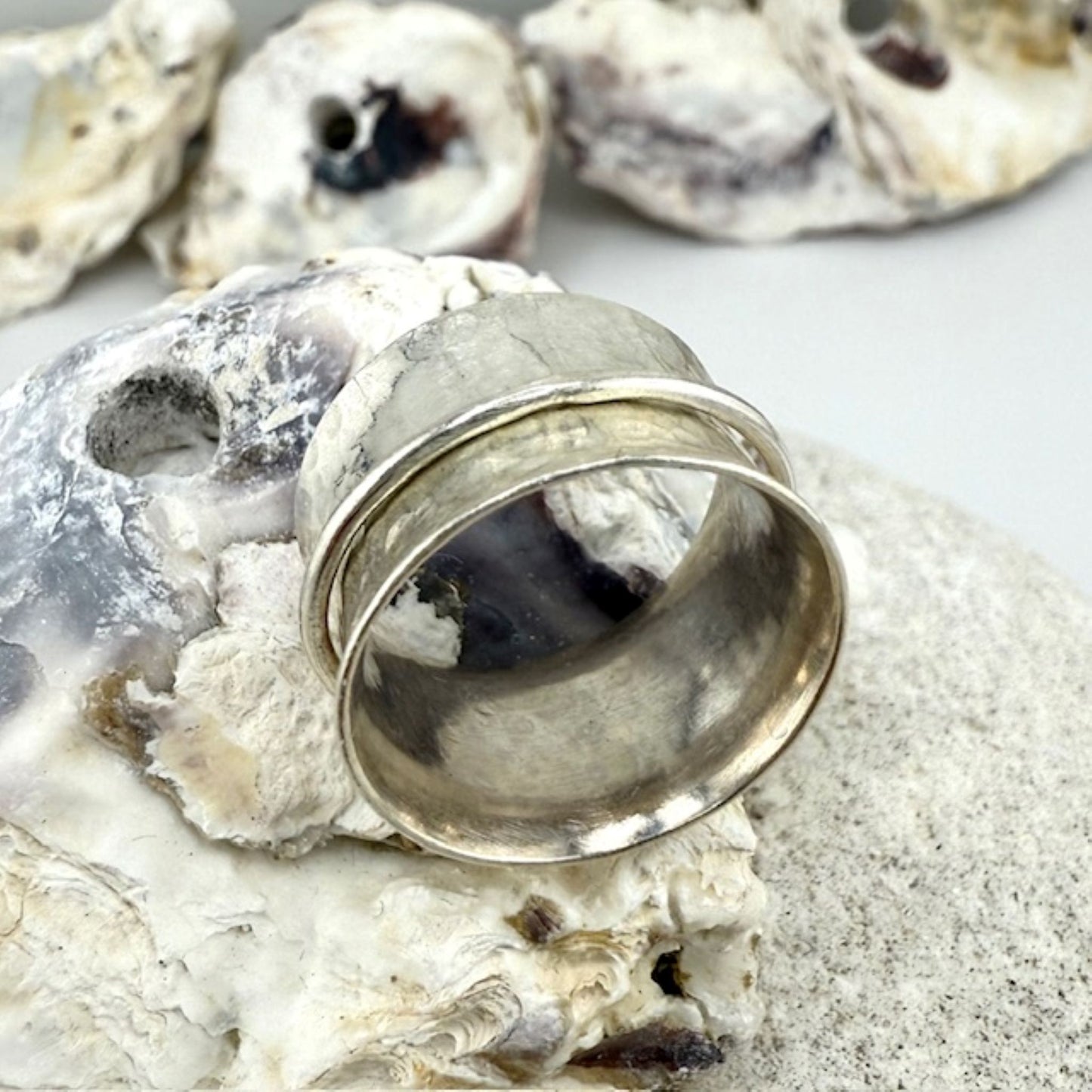 Silver spinner ring on a shell with sand in the background