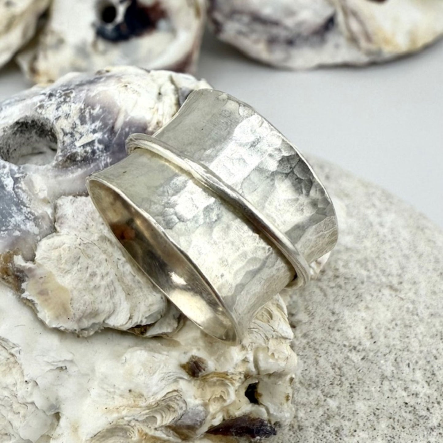 Silver spinner ring on a textured surface with shells in the background