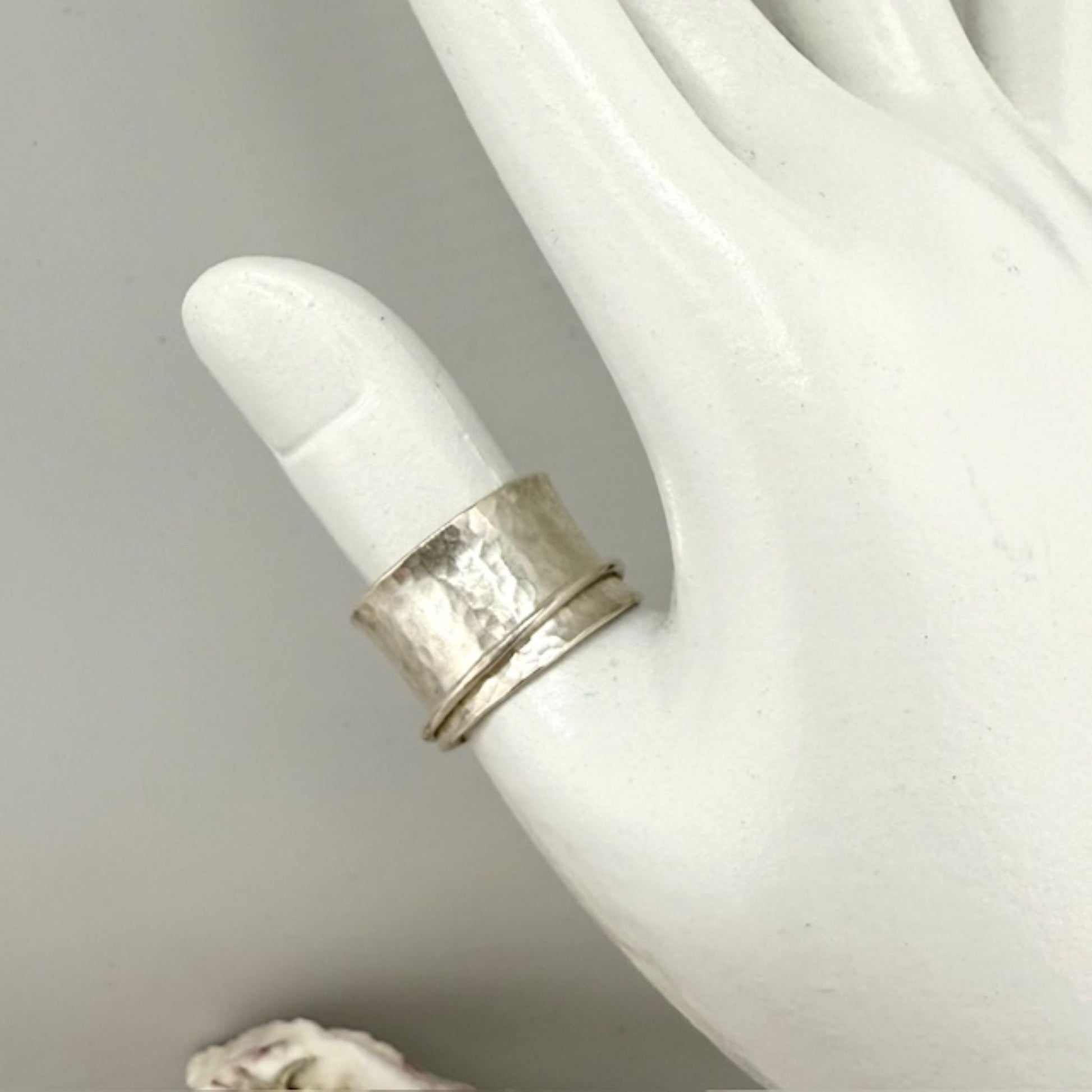 Silver spinner ring on a white mannequin finger against a neutral background